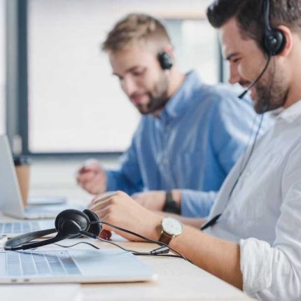 smiling young call center operators in headsets using laptops in office transformed